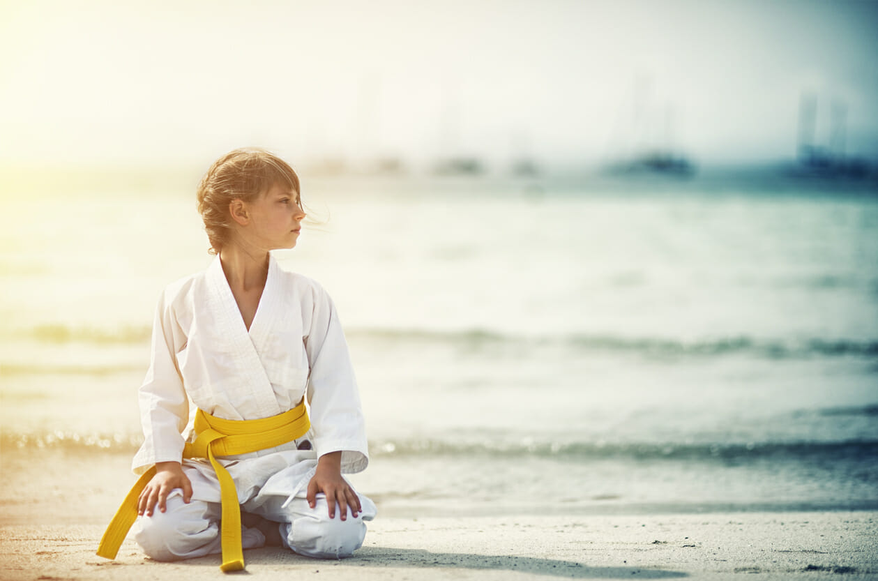 Little karate girl sitting in seiza on beach