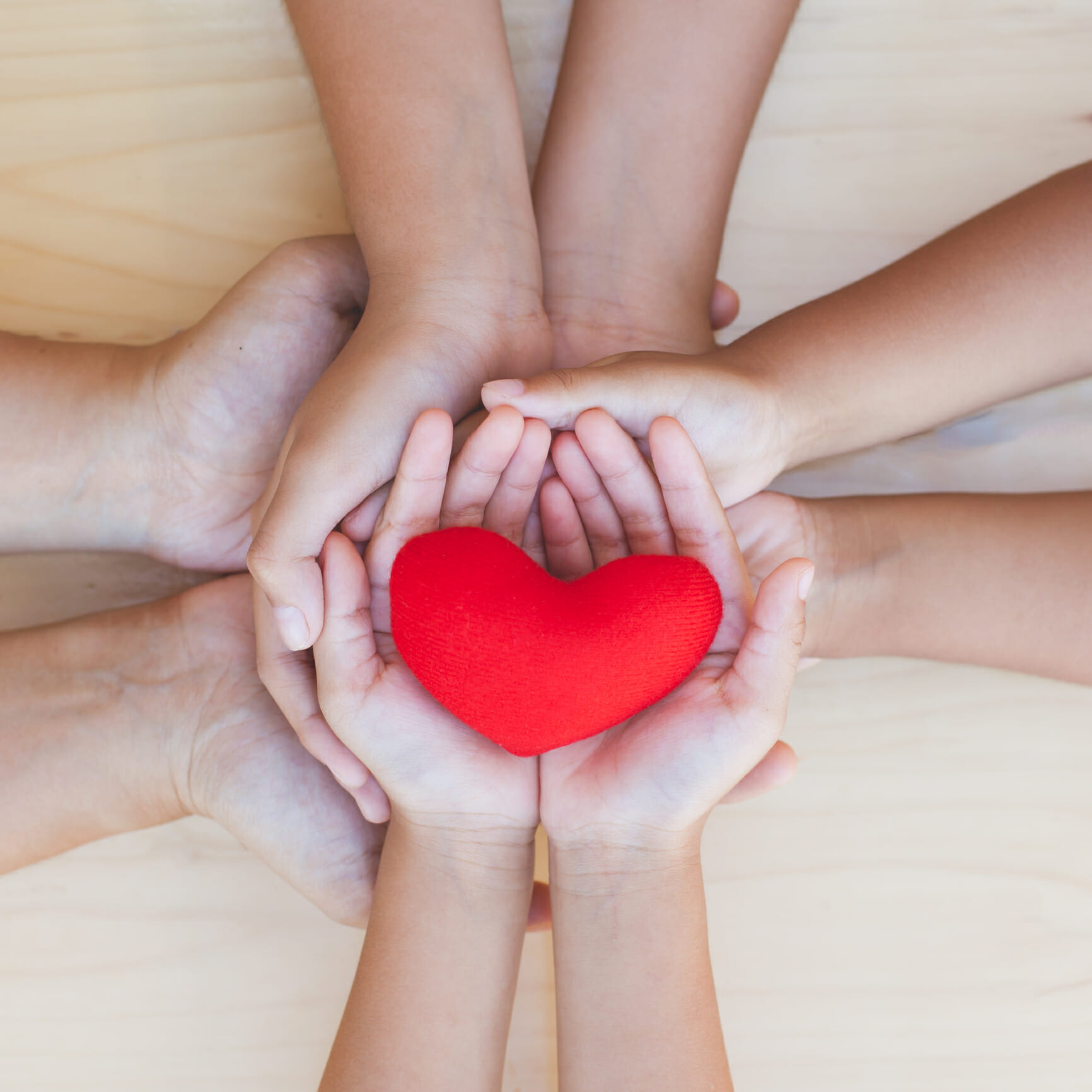 Red heart in parent and children holding hands together on wooden background